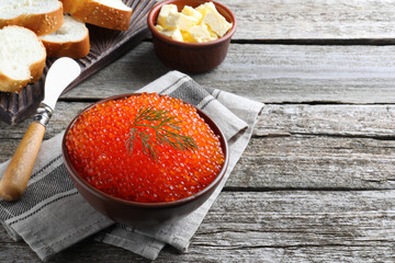 Bowl with delicious red caviar and dill on wooden table. Space for text