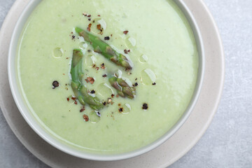 Delicious asparagus soup on light grey table, top view