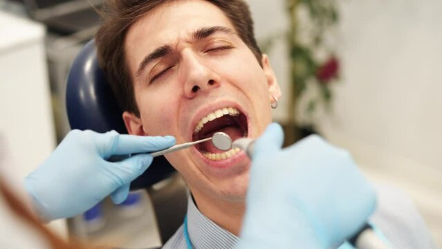 Dentist using dental instruments to check teeth sensitivity of male patient