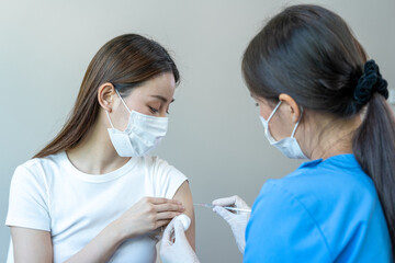 Asian woman wearing a medical mask receives coronavirus vaccine from a doctor. People are vaccinated against COVID-19 to prevent infection with the virus and stop its spread.