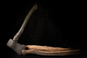 Antique camping hatchet, axe standing vertical stuck in fire wood with dark background and deer antler.