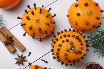 Pomander balls made of tangerines with cloves and fir branches on white wooden table, flat lay
