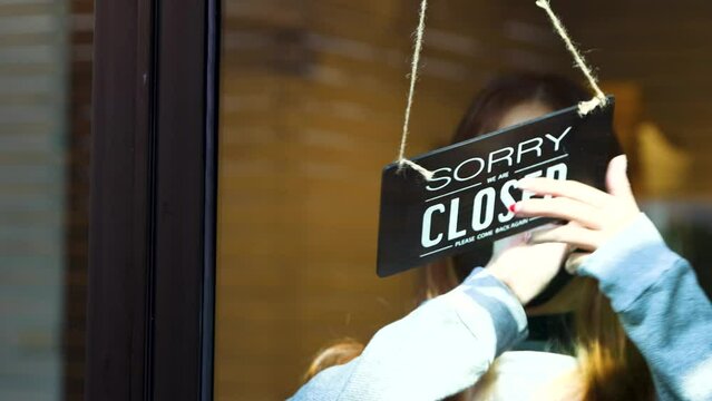 Sorry we're closed. A woman turn open sign to closed sign on glass door and turn off the light. Realtime Video 4k