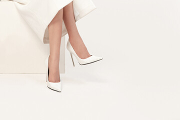 Young woman in a simple white dress, white shoes, sitting cross-legged, isolated on white background
