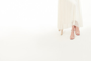 Young woman in a simple white dress, white shoes, sitting cross-legged, isolated on white background