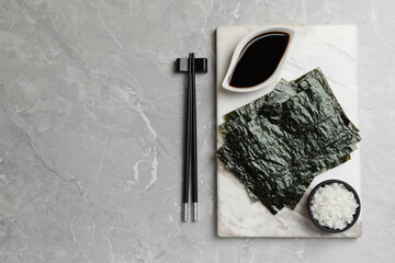 Dry nori sheets, rice, soy sauce and chopsticks on light grey marble table, flat lay. Space for text