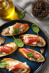 Delicious bruschettas with cheese, prosciutto and slices of black truffle on grey table, flat lay