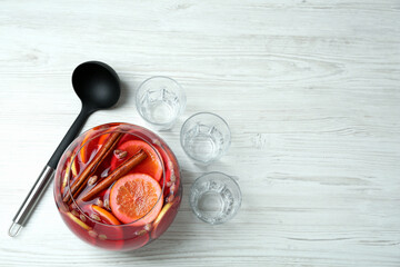 Empty glasses and ladle near bowl of aromatic punch drink on white wooden table, flat lay. Space for text