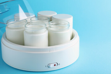 Modern yogurt maker with full jars on light blue background