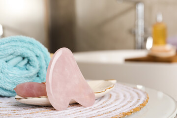 Rose quartz gua sha tool, natural face roller and towel on table in bathroom, closeup. Space for text