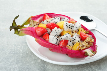 Yummy pitahaya boat with mango, granola and strawberry on light grey table, closeup