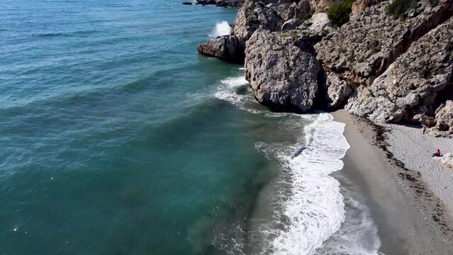 People sunbathing on Carabeo beach in the city center of Nerja. Huge rocks on a beach in the south part of Spain. Popular tourist destination in Andalusia Spain. Waves crashing in on the beach.