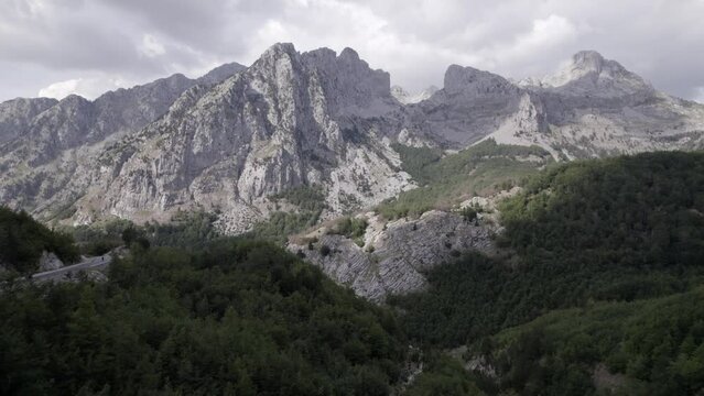 Frontal plane drone video moving over Sh 21 in albania with Mount Korab in front as the main shot. A motorcycle can be seen passing by the road, a drone flight reviews a tree closely.