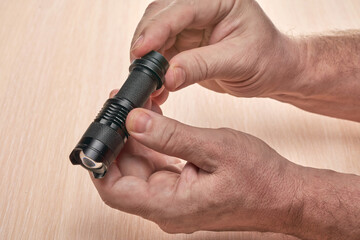 Hands hold a small black flashlight to replace the used battery - 485471062