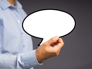 Hand holding of an empty white speech bubble against a gray background.
