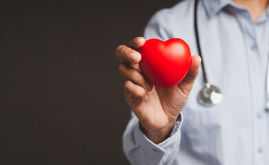Hand of a doctor holding a red heart shape while standing in the hospital or clinic.