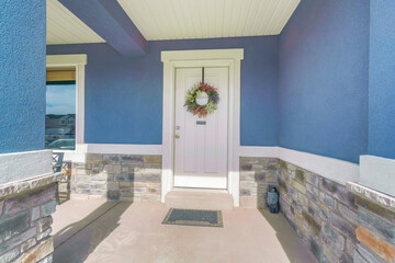 Porch of a blue house with white front door with wreath