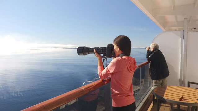 Cruise Ship Alaska Glacier Bay Tourists looking at landscape from private balcony suite stateroom cabin using telelens camera and binoculars. People on vacation travel looking at wildlife cruising