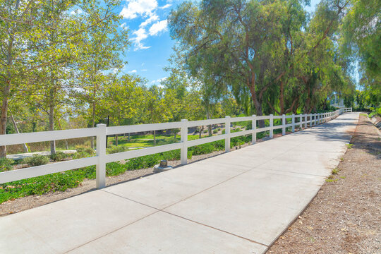 Small concrete path with white fence barrier and trees at Ladera Ranch in South California