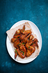 White plate of barbecue chicken wings on blue background. Top view.
