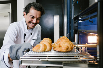 young Latin man baker and baking croissant and bread on oven at kitchen in Mexico Latin America