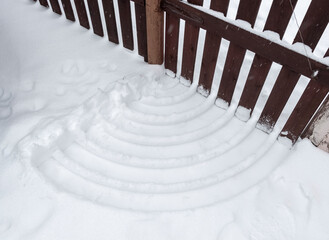 Furrows in the snow in the shape of a Wi-Fi icon from a wooden gate in the backyard of a private...
