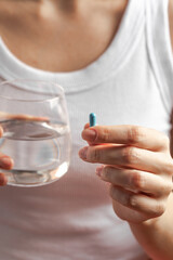 
Tablet in hand, glass of water in the background. Medicine, vitamins, women's health.