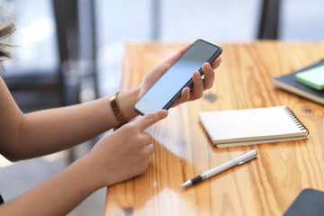 Close-up shot, A woman holding a smartphone over wooden table.
