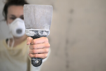 A woman worker holds a tool dirty putty knife  for  the leveling walls in her hand, makes repairs in the house

