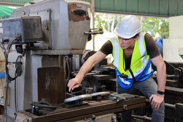 Technician engineer or worker in protective uniform standing and using computer while controlling operation or checking industry machine process with hardhat  at heavy industry manufacturing factory