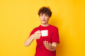 Young curly-haired man posing with a white mug and in the hands of a drink yellow background unaltered