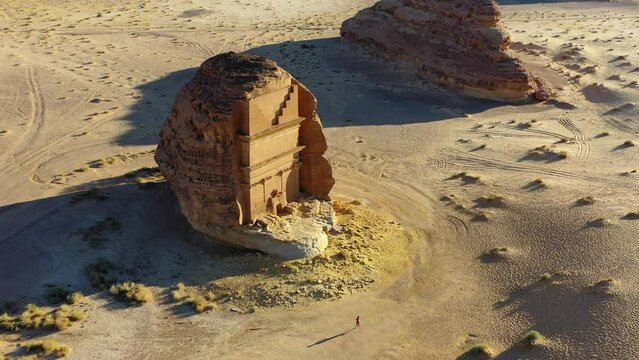 Aerial view of a man running at the Hegra monument, sunny evening, Al Madinah Region in the Hejaz, Saudi Arabia - tilt, drone shot