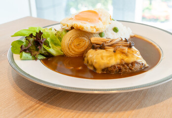 Close up Japanese Burger and curry with white rice, topped with cheese, Shimeji mushroom, fried egg. Food on a white round plate with fresh salad.