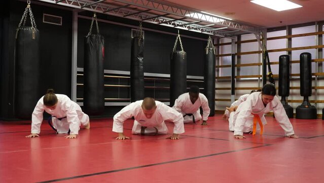 Men and women wearing kimono and doing push-ups in gym during group karate training.