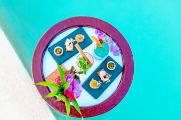 served floating tray in swimming pool with drinks and snacks on tropical island resort in Maldives, cocktails and canapes for romantic date or honeymoon in luxury hotel, travel concept