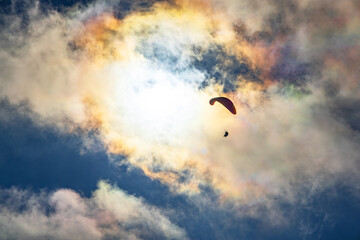 Paragliding adventure sport against bright sun on cloudy sky