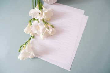 Obraz na płótnie Canvas A blank letter paper with white freesia flowers and vase on white pale green background. Mother’s Day, Women7s day, Father’s Day, weeding celebration background.
