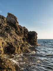 Rocky coast near the sea. Sea waves crash against the rocks. Sharp rocks. Horizon line between sky and sea. Beautiful landscape. Vertically.