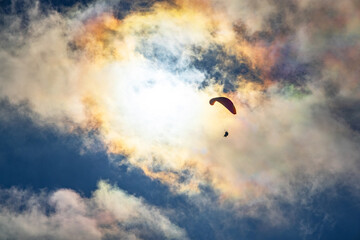 Naklejka na ściany i meble Paragliding adventure sport against bright sun on cloudy sky