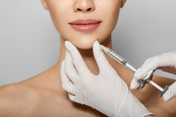 Syringe near woman's chin, beauty injections with fillers for chin shape correction. Cropped female face while procedure chin contouring - 485483298