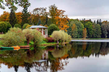 Fototapeta premium Rotunda on the shore of a quiet lake against the backdrop of an autumn foliage forest in Latvia. oncept of a relaxing weekend holiday in nature.