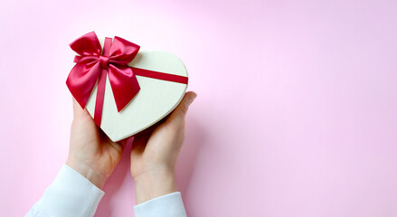 Womans hands holding gift box with red ribbon on pink background, copy space. Valentine's Day, spring holidays, Christmas and birthday concept. Flat lay, top view.