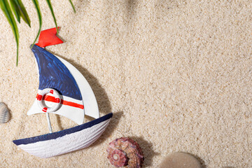 Toy boat and sea shells on white sea sand. Vacation concept by the sea with free space for text