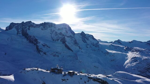 Picturesque winter Alpine landscape of snow-capped rocky ridge Gornergrat with observatory on summit and high pyramidal Matterhorn mountain in background on sunny day, Switzerland