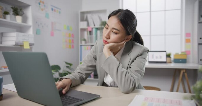 Young Asian businesswoman sit on desk with laptop overworked tired burnout syndrome at office. Exhausted lady with sleeply eye at workplace, Girl not enjoy unhappy with work, Work mental health.
