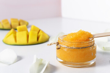 Cosmetic scrub for skin cleansing with pieces of ripe mango on a white table. Spa treatments and peeling with a sugary texture of the product.