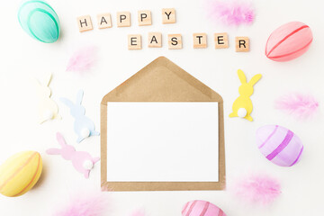 Mockup with white blank template for copy space, envelope for congratulations and greetings on a wooden table with Easter decorations, top view, flat lay.