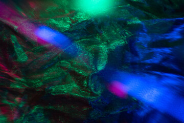 Obraz na płótnie Canvas Neon abstract background. Color lens flare. Creased foil texture. Blur green blue pink light flecks noise on dark shimmering wrinkled metal surface.