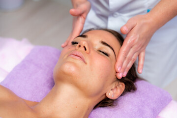 Fototapeta na wymiar Relaxing massage. European woman getting facial massage in spa salon, side view
