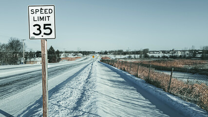 Speed limit sign and winter landscape with snow covered road and sidewalk